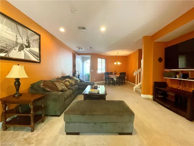 Living area with visible vents, baseboards, a chandelier, stairway, and carpet flooring