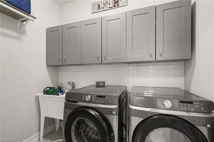 Laundry area with washing machine, dryer, mud sink, and gray cabinetry