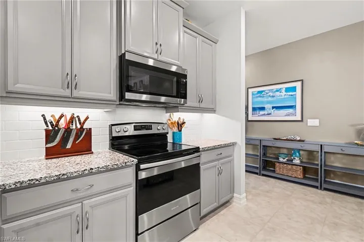 Kitchen featuring stainless steel appliances, light stone counters, decorative backsplash, light tile patterned floors, and gray cabinetry