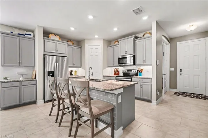 Kitchen featuring gray cabinets, stainless steel appliances, a kitchen bar, and recessed lighting