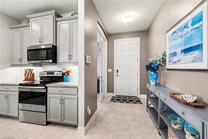 Kitchen with gray cabinetry, stainless steel appliances, light stone counters, light tile patterned flooring, and decorative backsplash