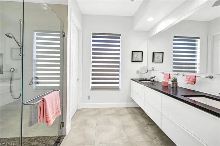 Full bathroom with double vanity, baseboards, a stall shower, and a sink