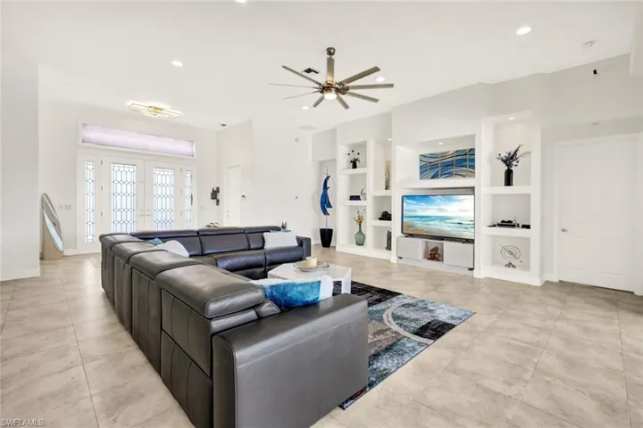 Tiled living room with built in shelves, a ceiling fan, baseboards, recessed lighting, and french doors