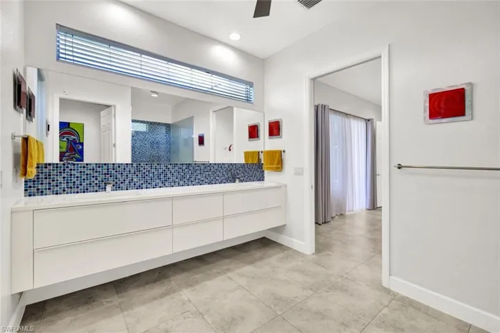 Full bathroom featuring a ceiling fan, a shower, tasteful backsplash, double vanity, and baseboards