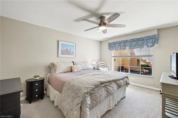 Bedroom with ceiling fan, privacy blinds and light colored carpet