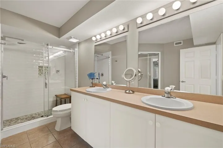 Bathroom with tile patterned flooring, dual vanity, toilet, and an enclosed shower