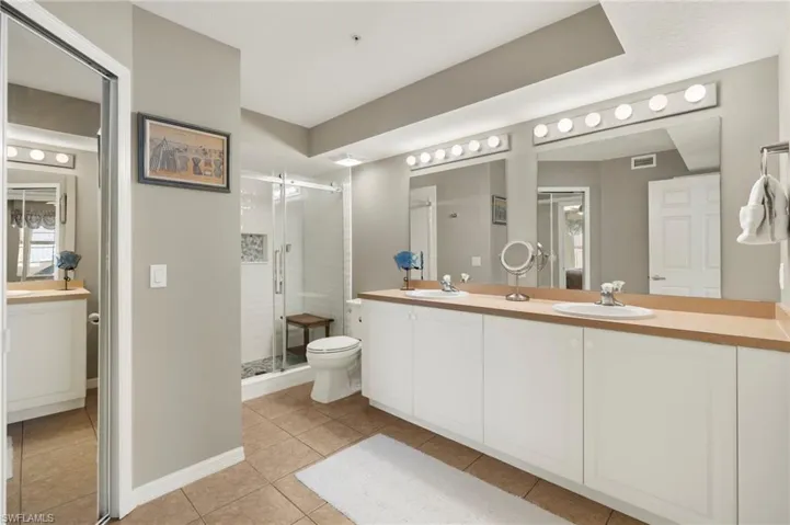 Bathroom featuring tile patterned floors, dual vanity, an enclosed shower, and toilet