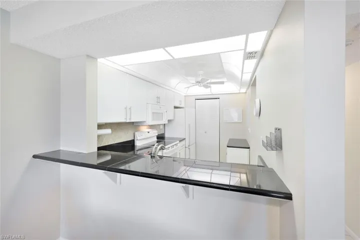 Kitchen with tasteful backsplash, white cabinets, white appliances, kitchen peninsula, and ceiling fan