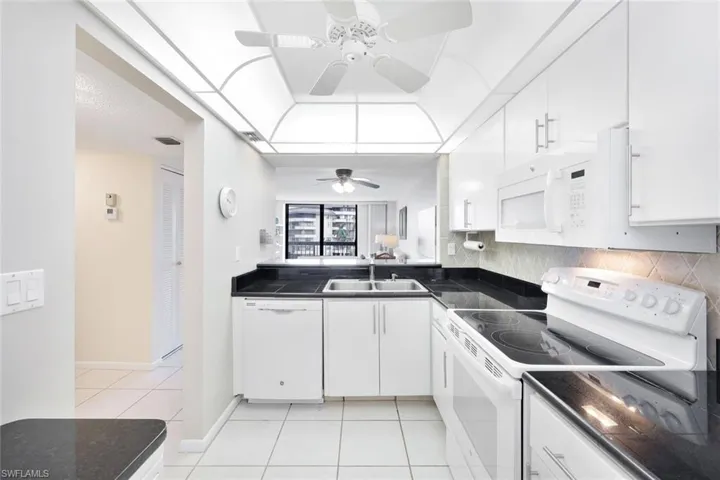 Kitchen with white appliances, light tile patterned floors, white cabinets, ceiling fan, and sink