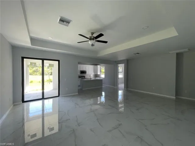 Unfurnished living room featuring a raised ceiling and ceiling fan