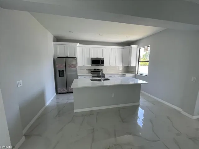 Kitchen with appliances with stainless steel finishes, a center island, sink, and white cabinetry