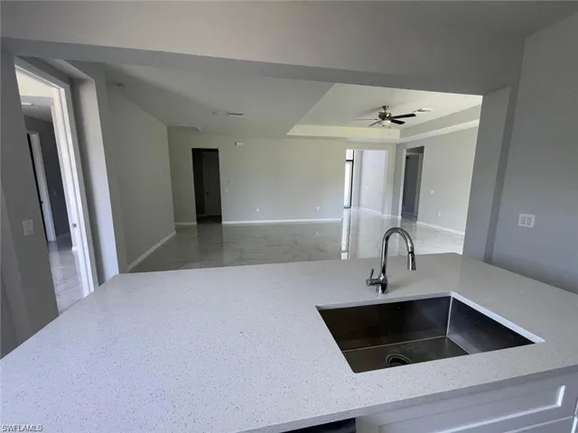 Kitchen featuring ceiling fan, light stone countertops, and sink