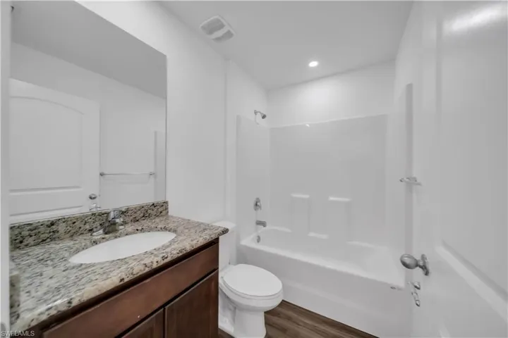 Full bathroom with shower / bathtub combination, vanity, dark wood-type flooring, and recessed lighting