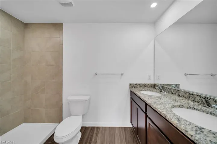 Full bathroom featuring double vanity, dark wood-style floors, a tile shower, and recessed lighting