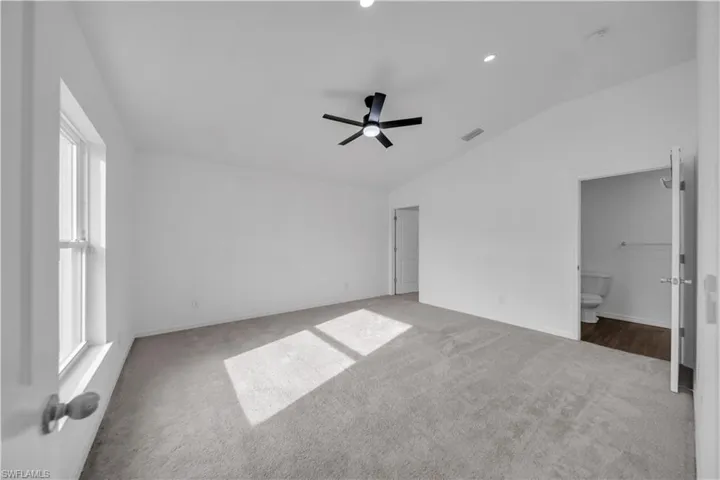 Unfurnished bedroom with vaulted ceiling, carpet floors, ceiling fan, and connected bathroom