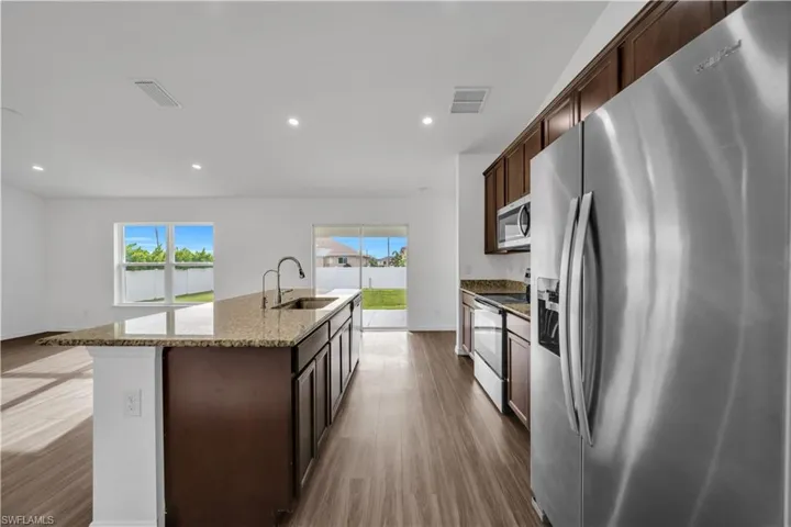 Kitchen with appliances with stainless steel finishes, dark brown cabinets, light stone countertops, dark wood-style flooring, and recessed lighting