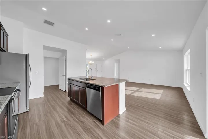 Kitchen with open floor plan, stainless steel appliances, light wood-style floors, recessed lighting, and decorative light fixtures