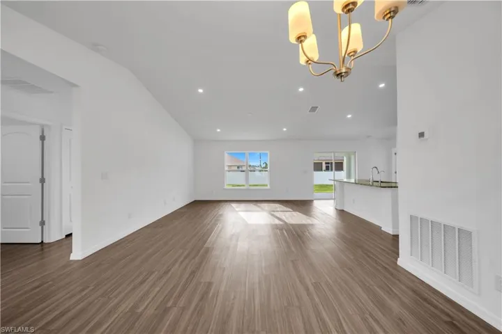 Unfurnished living room featuring recessed lighting, dark wood-style floors, lofted ceiling, and a chandelier