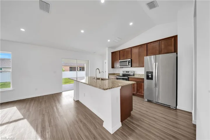 Kitchen featuring appliances with stainless steel finishes, an island with sink, dark wood-style floors, light stone countertops, and recessed lighting
