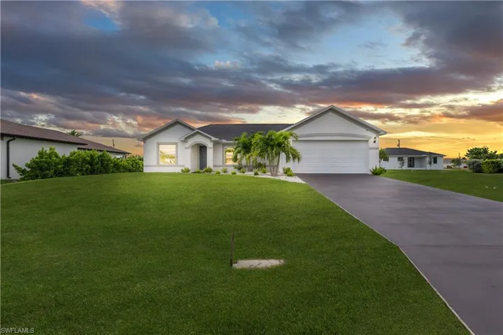 Ranch-style home with stucco siding, driveway, a lawn, and a garage