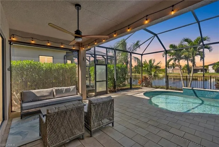 Pool at dusk with a patio area, a sunroom, a lanai, and a water view