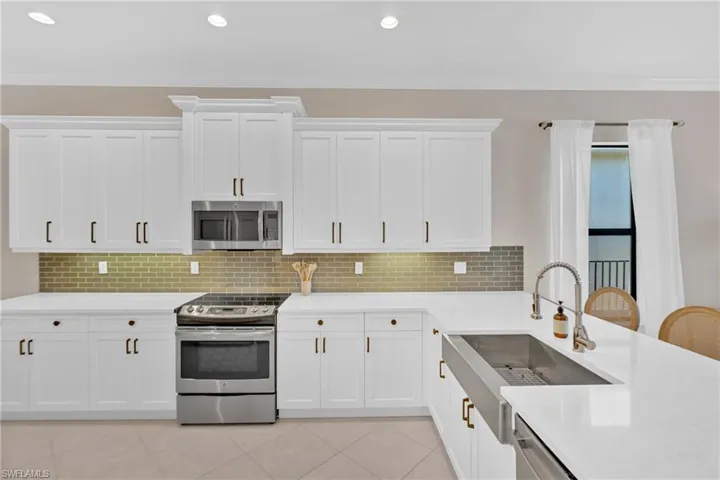 Kitchen with stainless steel appliances, tasteful backsplash, white cabinets, light stone counters, and recessed lighting