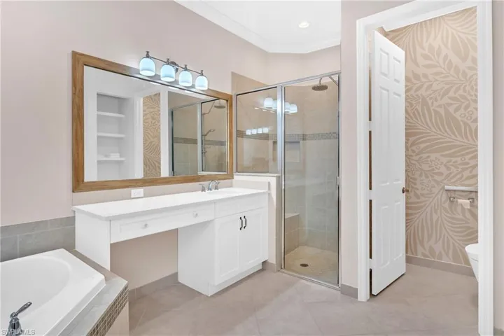 Full bath with a shower stall, vanity, light tile patterned floors, a bath, and ornamental molding