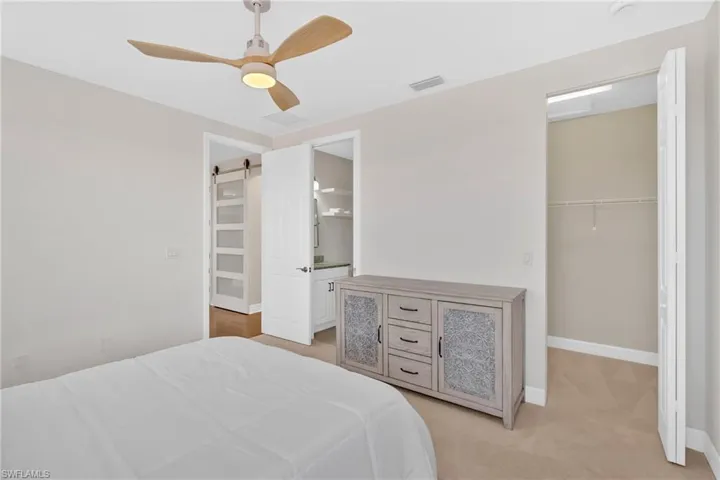 Bedroom with a barn door, ceiling fan, a walk in closet, light carpet, and ensuite bathroom