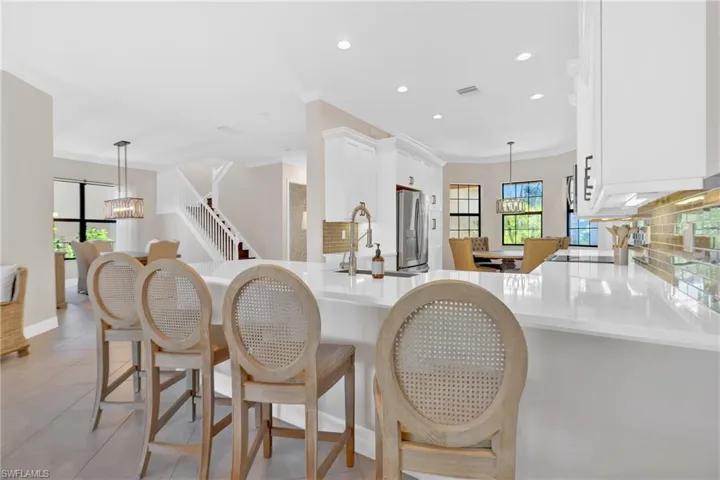 Kitchen featuring tasteful backsplash, white cabinetry, crown molding, a breakfast bar, and hanging lights