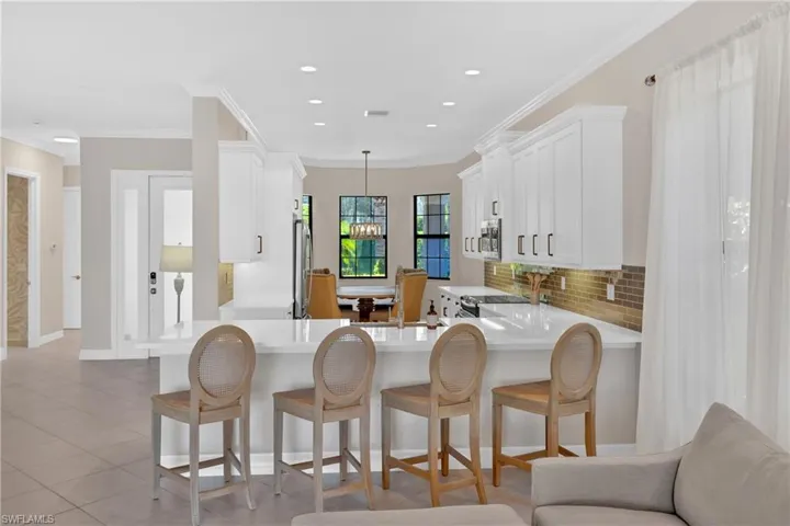 Kitchen with a kitchen breakfast bar, white cabinets, crown molding, decorative backsplash, and light stone counters