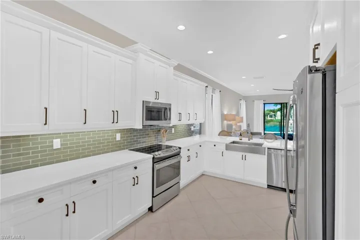 Kitchen featuring stainless steel appliances, white cabinetry, crown molding, light stone counters, and recessed lighting