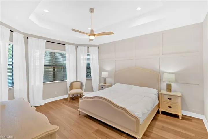 Bedroom with a decorative wall, light wood finished floors, ceiling fan, recessed lighting, and a tray ceiling