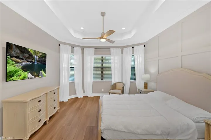Bedroom with light wood finished floors, a ceiling fan, recessed lighting, crown molding, and a tray ceiling