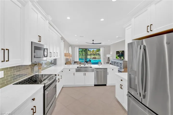 Kitchen featuring stainless steel appliances, open floor plan, white cabinets, recessed lighting, and ornamental molding
