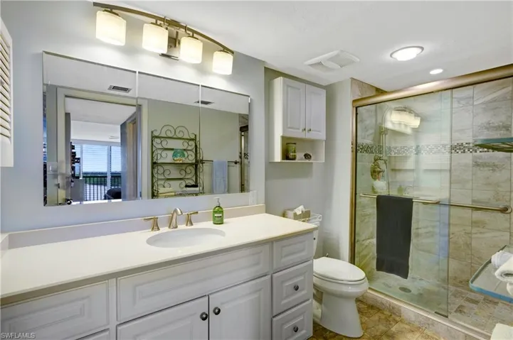 Primary bath with newer vanity, light/plumbing fixtures, custom tiled shower, & glass shower door.
