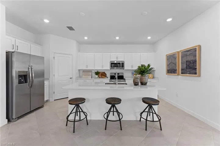Kitchen featuring stainless steel appliances, white cabinets, an island with sink, a kitchen breakfast bar, and recessed lighting