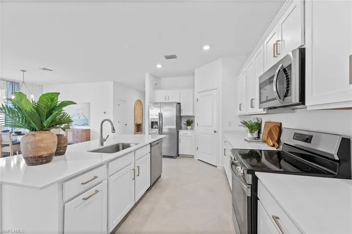 Kitchen with appliances with stainless steel finishes, an island with sink, white cabinets, light countertops, and recessed lighting