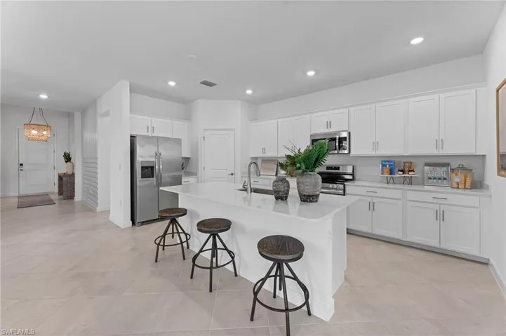 Kitchen with stainless steel appliances, a breakfast bar, white cabinetry, a center island with sink, and light countertops