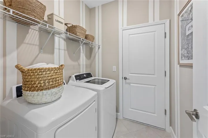 Laundry room with washer and clothes dryer and light tile patterned floors