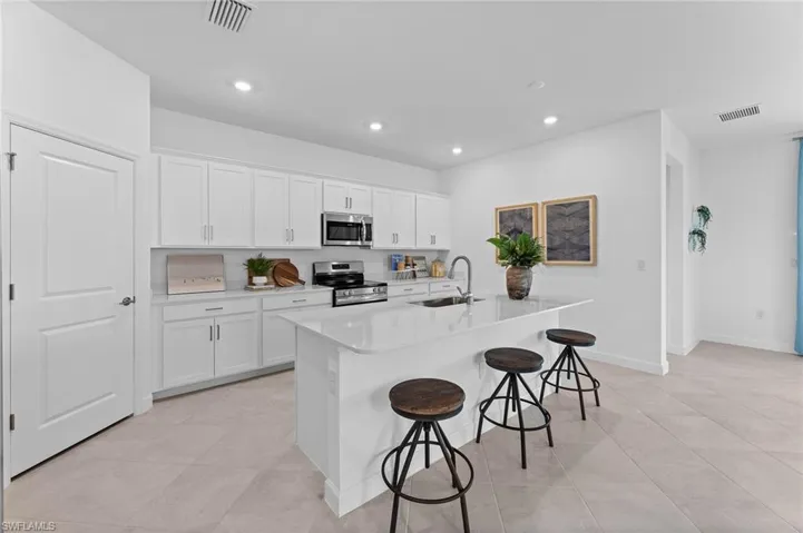 Kitchen with a breakfast bar area, stainless steel appliances, recessed lighting, a center island with sink, and light countertops