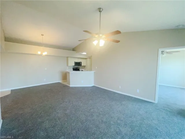 Unfurnished living room featuring ceiling fan with notable chandelier, dark colored carpet, and lofted ceiling