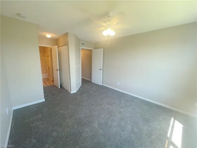 Unfurnished bedroom featuring a closet, ensuite bath, ceiling fan, and dark carpet