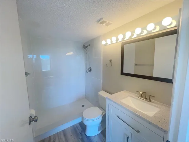 Bathroom featuring wood-type flooring, a tile shower, vanity, a textured ceiling, and toilet