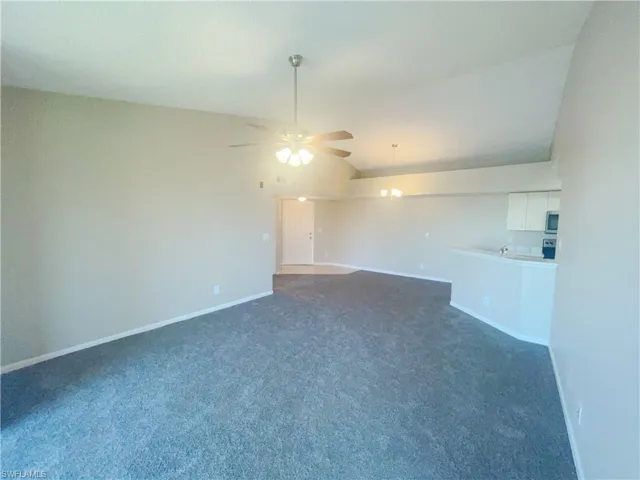 Carpeted spare room featuring vaulted ceiling and ceiling fan