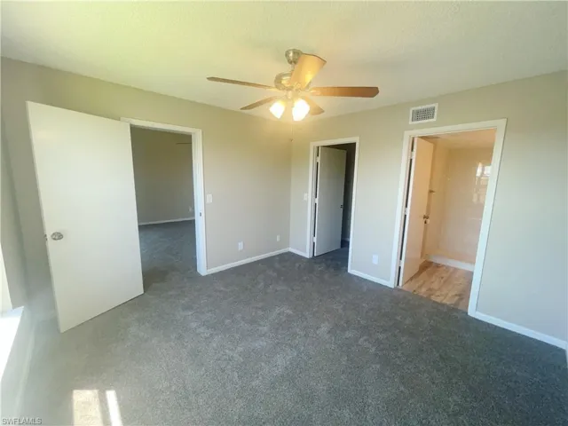Unfurnished bedroom with a textured ceiling, dark colored carpet, ceiling fan, and connected bathroom