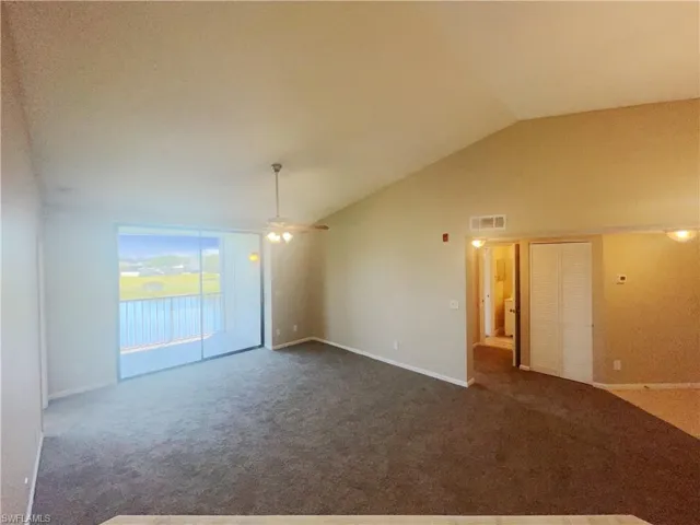 Carpeted empty room featuring ceiling fan and lofted ceiling