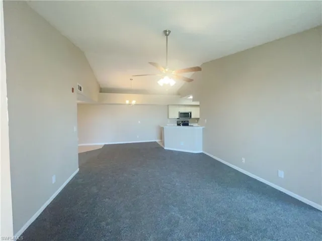 Unfurnished living room with ceiling fan, dark colored carpet, and lofted ceiling