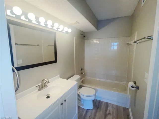 Full bathroom featuring toilet, tiled shower / bath combo, vanity, and hardwood / wood-style flooring