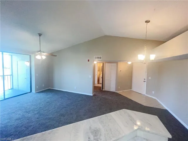 Unfurnished living room with lofted ceiling, ceiling fan with notable chandelier, and carpet floors