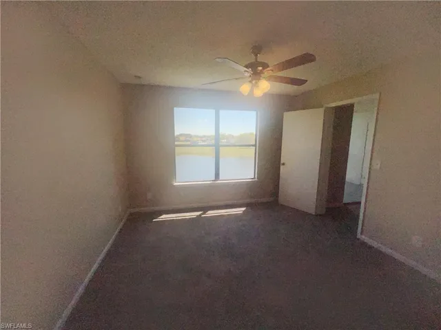 Unfurnished bedroom with a water view, dark carpet, and ceiling fan